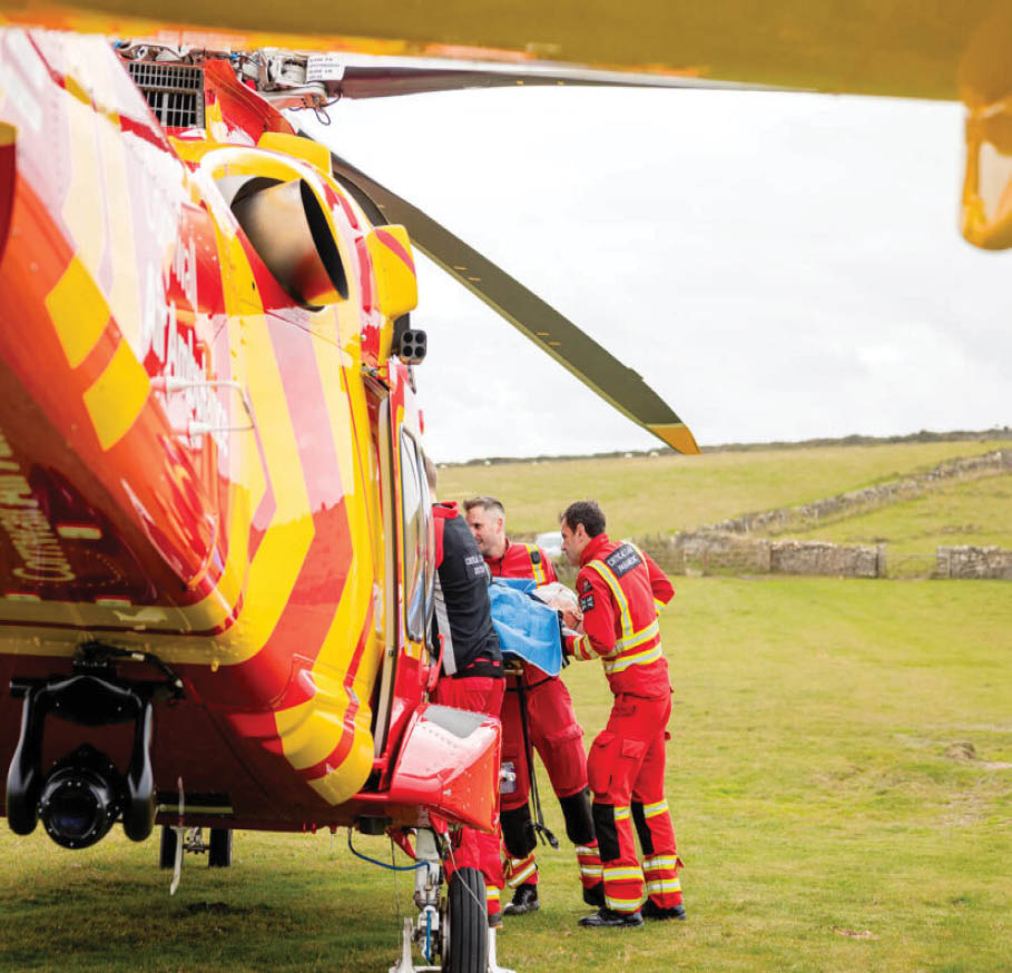 A group of people in red and yellow rescue uniforms are gathered near a red and yellow helicopter on a grassy field. Description generated by AI
