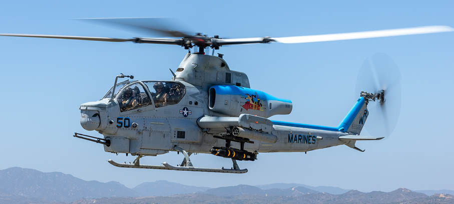 A military helicopter with spinning rotors is flying against a clear blue sky. Description generated by AI