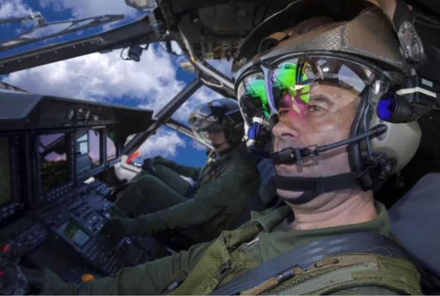 Two people wearing helmets and headsets are seated inside a cockpit with multiple control panels and screens. Description generated by AI