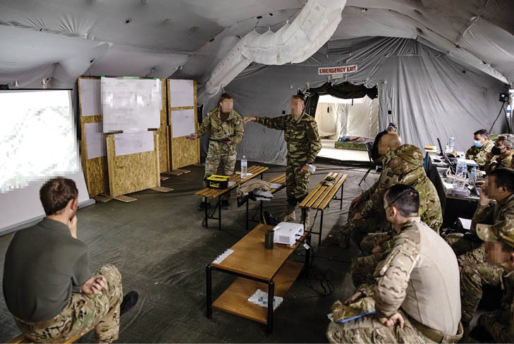 A group of soldiers are gathered in a tent, watching a presentation on a large screen. There are several chairs and dining tables in the room, and a man is pointing at the screen. The soldiers are engaged and focused on the presentation. AI generated content
