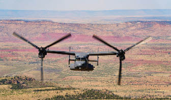 A helicopter with two large blades flying over a desert landscape. Description generated by AI