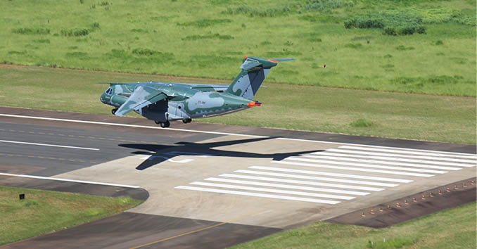 A green airplane is flying low over a runway. Description generated by AI