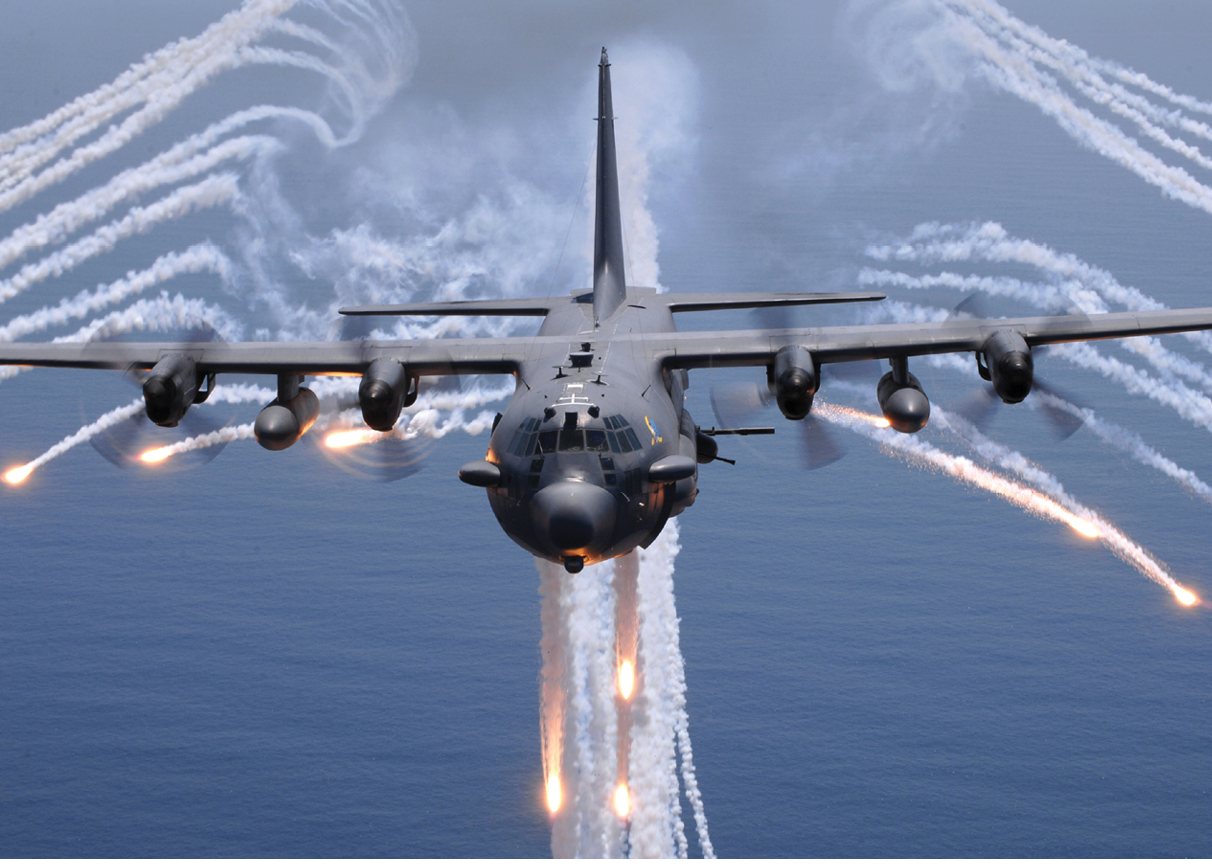 A military plane is flying through the sky with a trail of smoke behind it. Description generated by AI