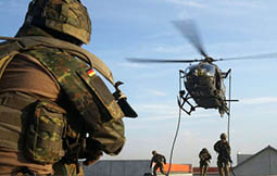 A man in a camouflage uniform is watching a helicopter. Description generated by AI