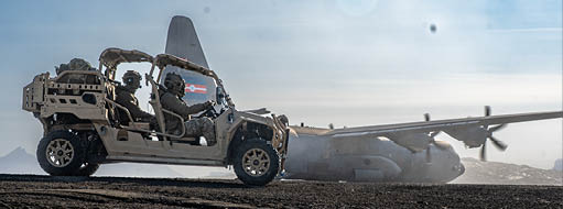 A military vehicle is driving on a dirt road next to a plane. Description generated by AI