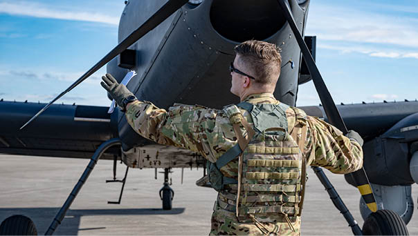 A man in camouflage standing in front of a helicopter. Description generated by AI