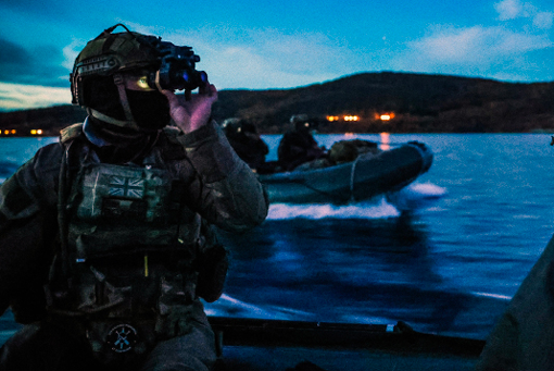 A man wearing a camouflage uniform is looking through binoculars at a boat. Description generated by AI
