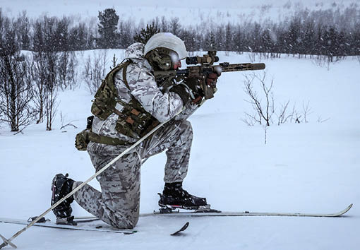 A man in camouflage pants and a helmet is holding a gun and pointing it at the ground. Description generated by AI