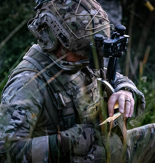 A man in a camouflage uniform is sitting in the grass. Description generated by AI