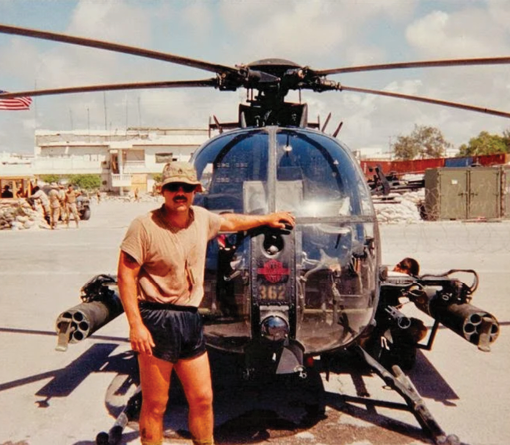 A man is standing in front of a helicopter. Description generated by AI