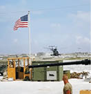 A man in a camouflage uniform stands in front of a flag. Description generated by AI