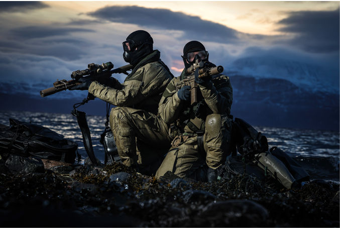 Two men in camouflage sitting on rocks with guns. Description generated by AI
