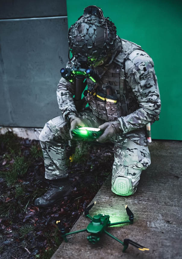 A man in camouflage pants and a helmet is kneeling down and looking at a green light. Description generated by AI