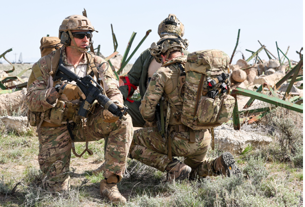 Two men in camouflage uniforms are sitting on the ground. Description generated by AI