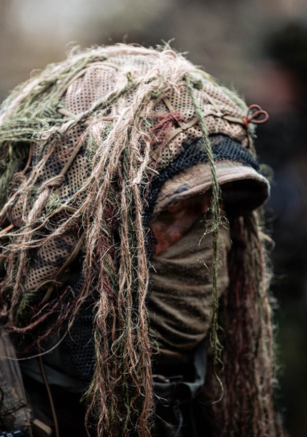 A man wearing a camouflage outfit with a hood on his head. Description generated by AI