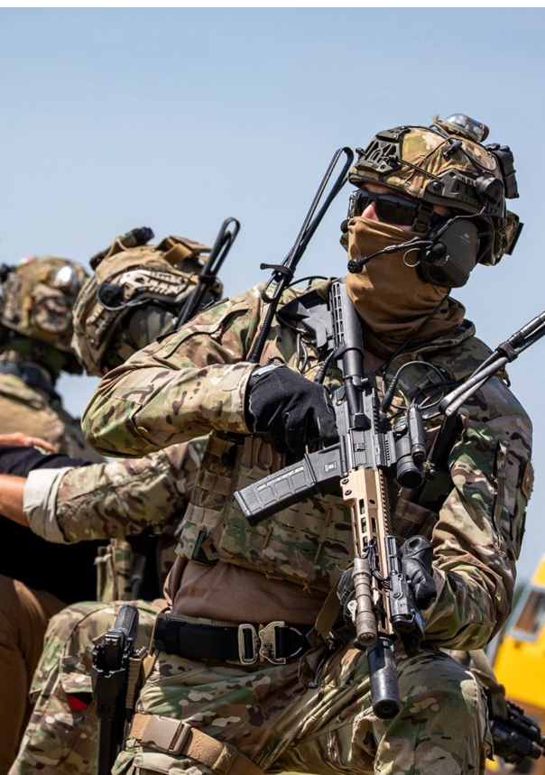 A man wearing a camouflage uniform with a gun on his back. Description generated by AI