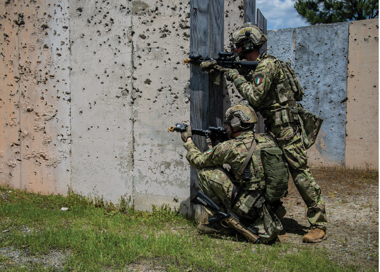 Two men in camouflage are playing a video game. Description generated by AI