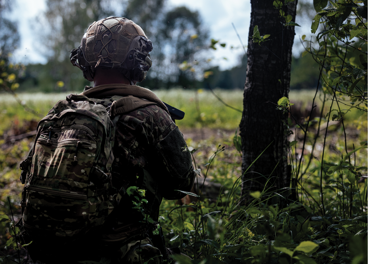 A man in a camouflage uniform is standing in a field. Description generated by AI