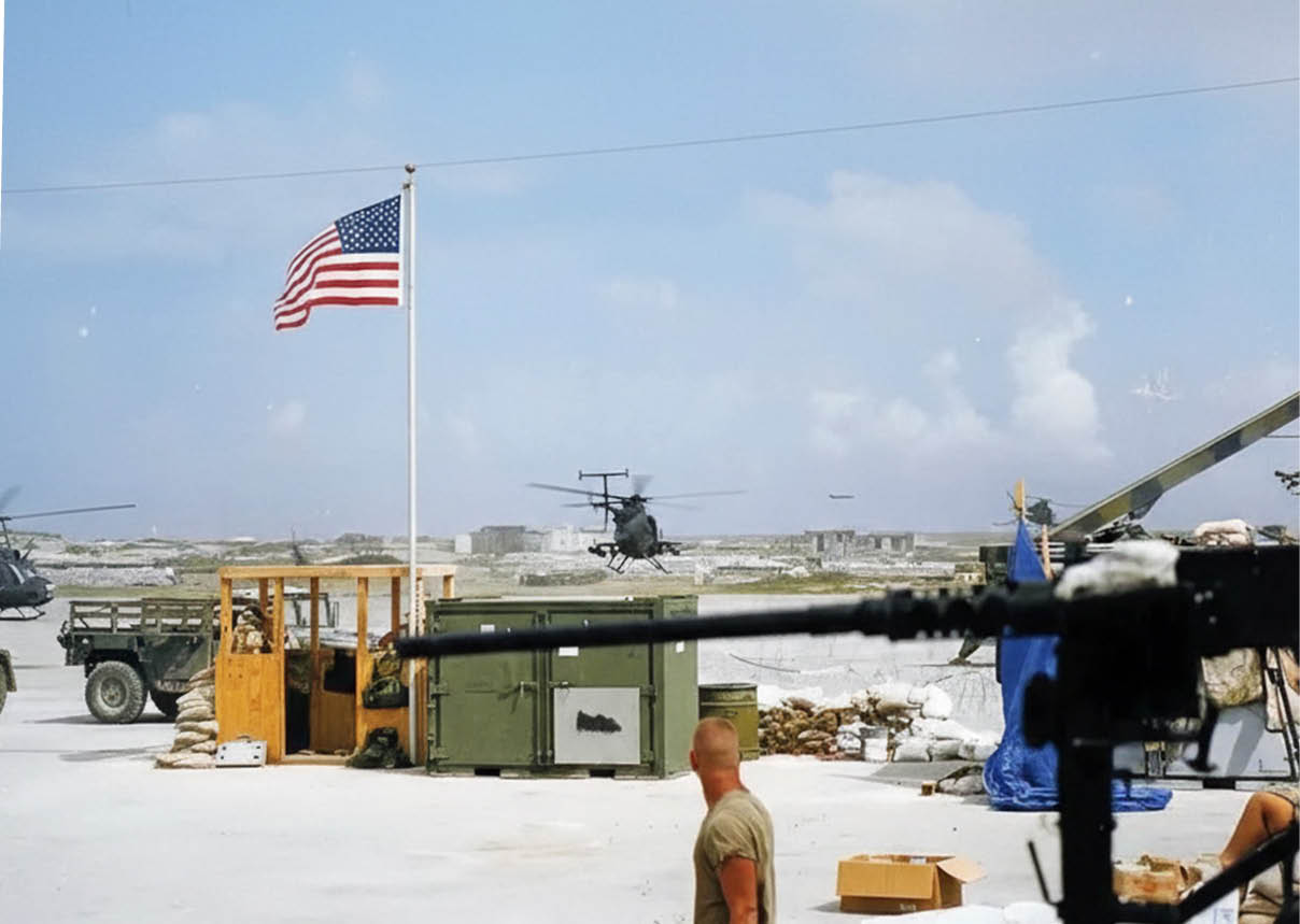 A man in a camouflage uniform stands in front of a flag. Description generated by AI
