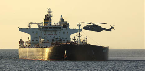A large cargo ship is sailing on calm water with a helicopter hovering just above its deck during sunset. Description generated by AI
