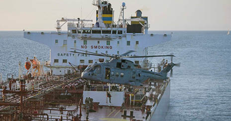 A helicopter is hovering above a large ship with people on its deck near the ocean. Description generated by AI