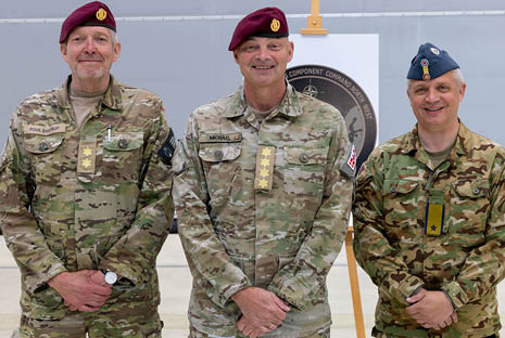 Three adults in military uniforms stand side by side indoors with two wearing maroon berets and one wearing a blue beret, all smiling and posing for the camera. Description generated by AI