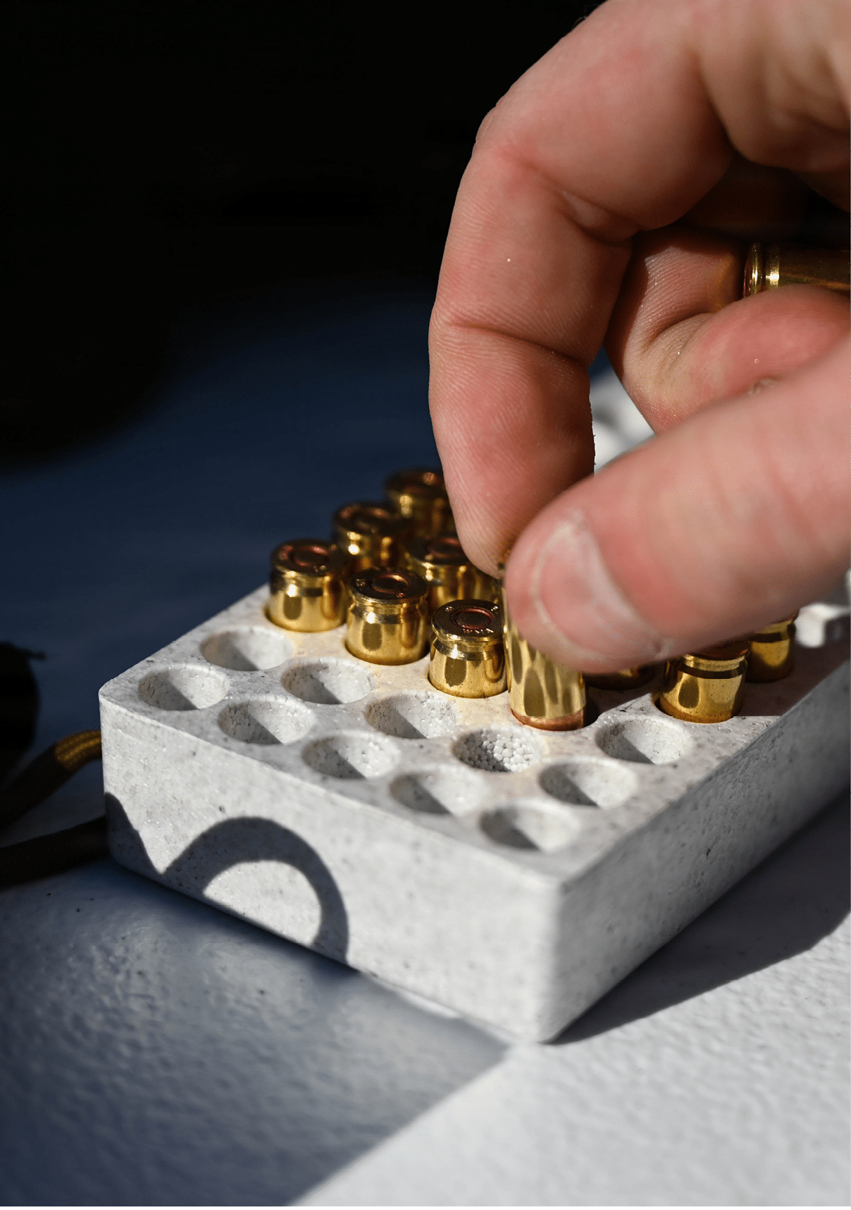 A hand is placing a small brass-colored bullet casing into a white tray with multiple circular slots. Description generated by AI