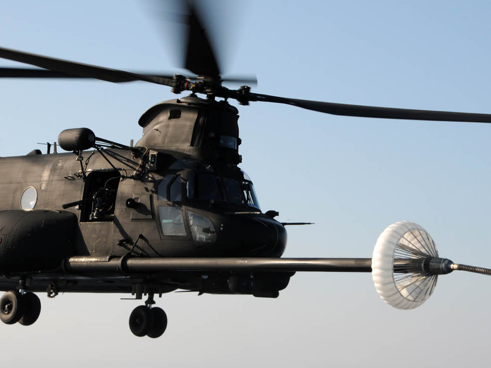 A black military helicopter is flying with its rotor blades spinning against a clear sky. Description generated by AI
