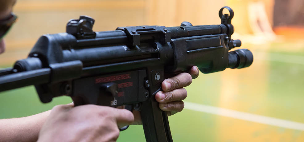 A person is holding and aiming a black rifle in an indoor shooting range. Description generated by AI