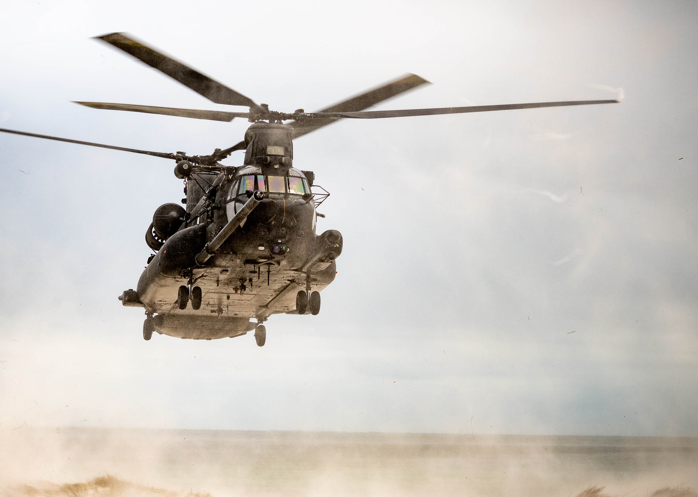 A large military helicopter is flying low against a cloudy sky with its rotor blades in motion. Description generated by AI