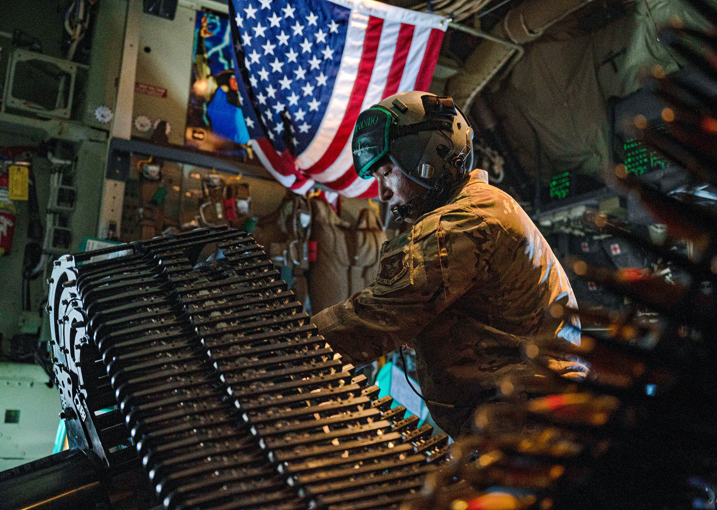 A person wearing a helmet and goggles is working inside a military vehicle with an American flag hanging in the background. Description generated by AI