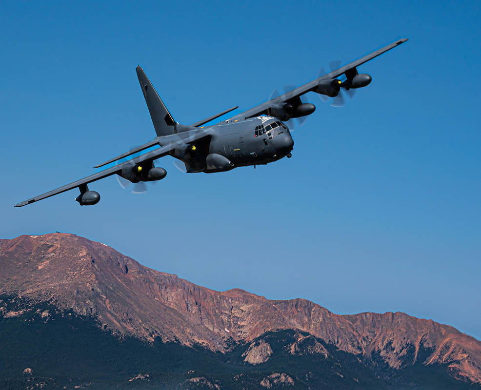 A military transport aircraft is flying low against a clear blue sky. Description generated by AI