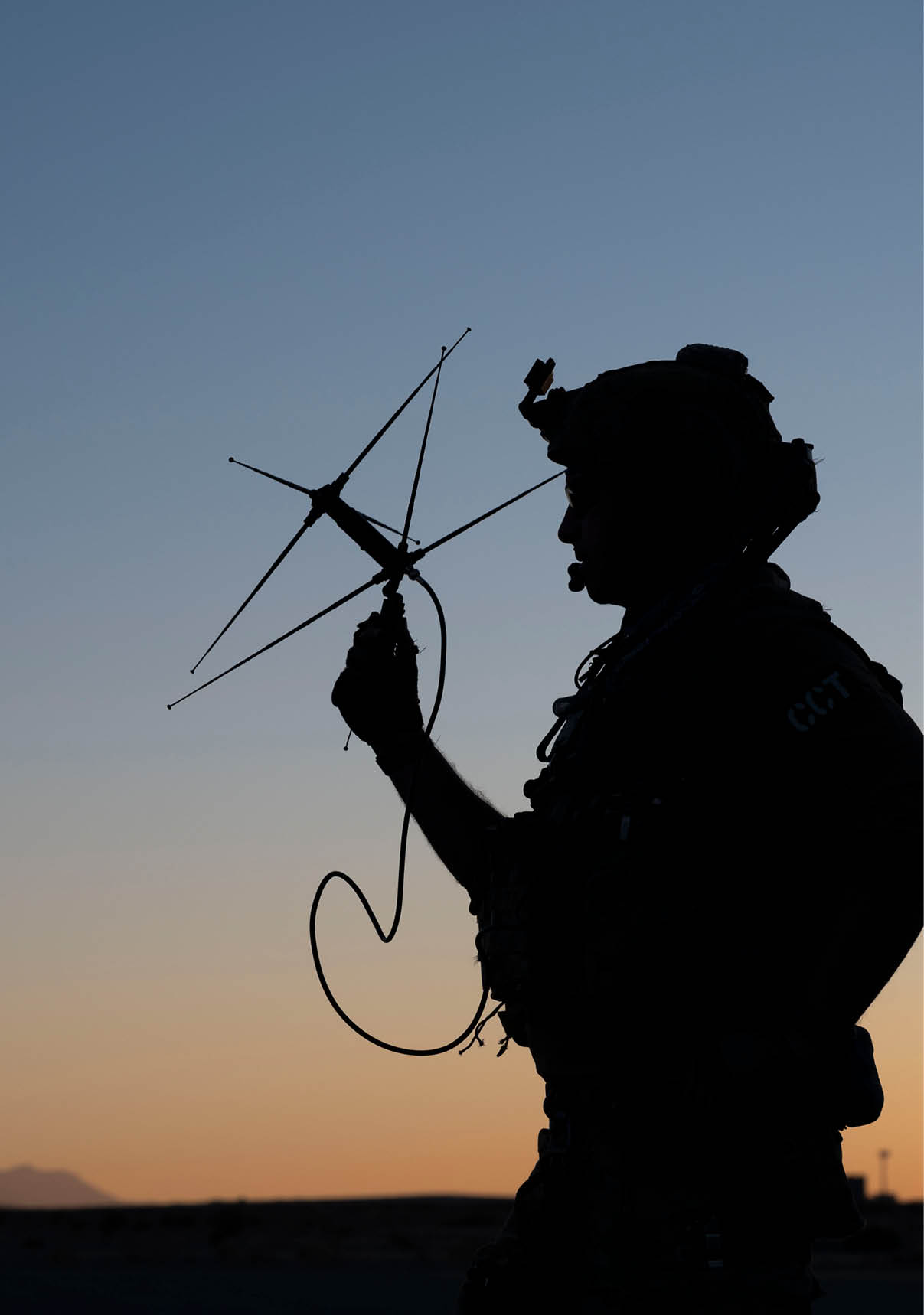 A person wearing tactical gear is holding and aiming a handheld antenna device against a sunset sky. Description generated by AI
