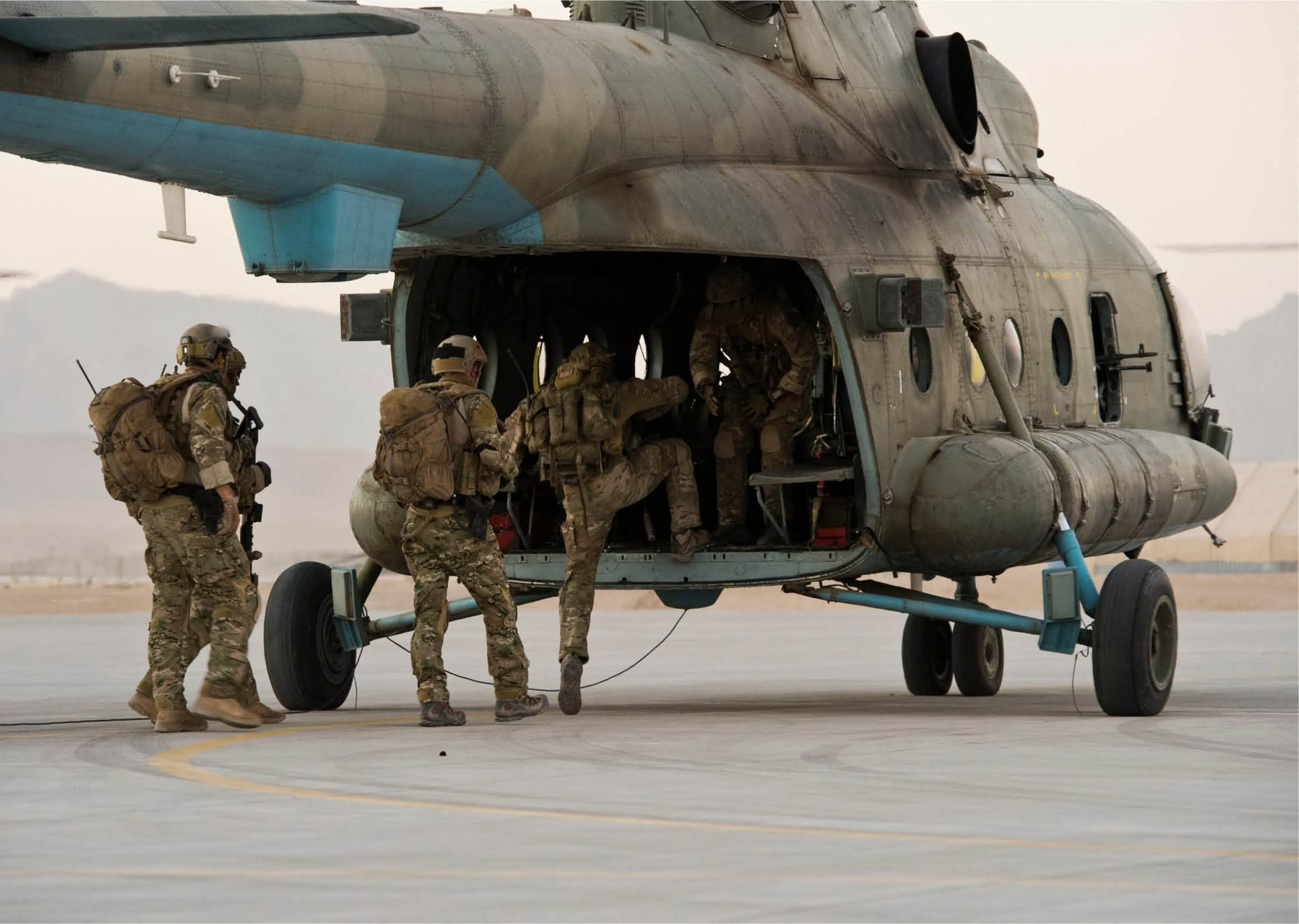 People in military uniforms are boarding a helicopter on a tarmac in a desert-like environment. Description generated by AI
