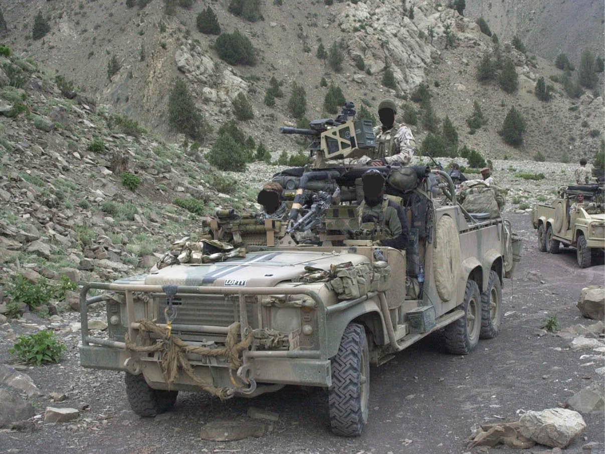 A military vehicle equipped with mounted weapons is driving on a rocky mountain road with several people in military uniforms inside and another similar vehicle following behind. Description generated by AI