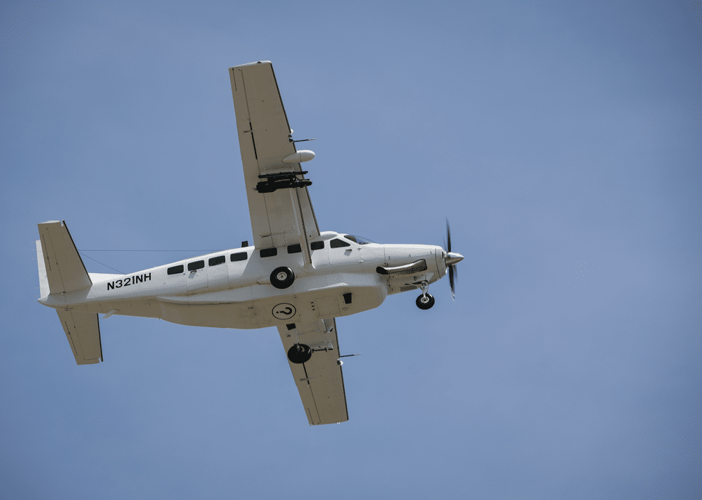 A white single-engine propeller airplane is flying against a clear blue sky. Description generated by AI