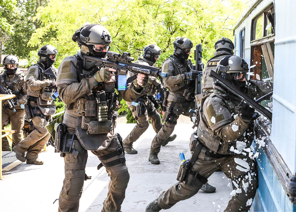 People dressed in tactical gear are crouching and holding firearms outdoors. Description generated by AI