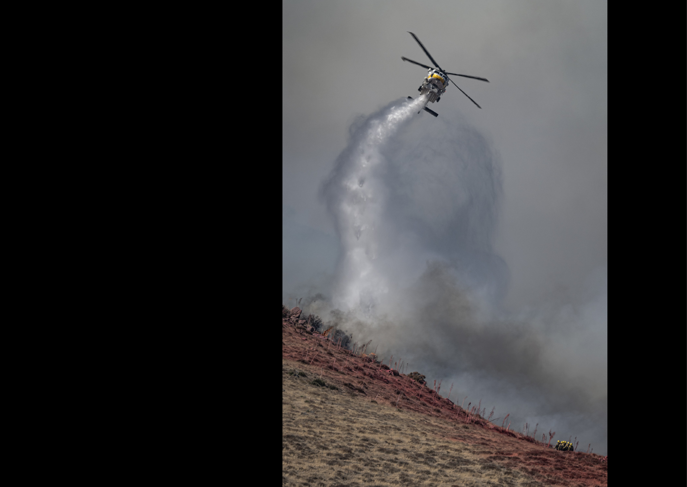 A helicopter is spraying water on a hillside, possibly to put out a fire. AI generated content
