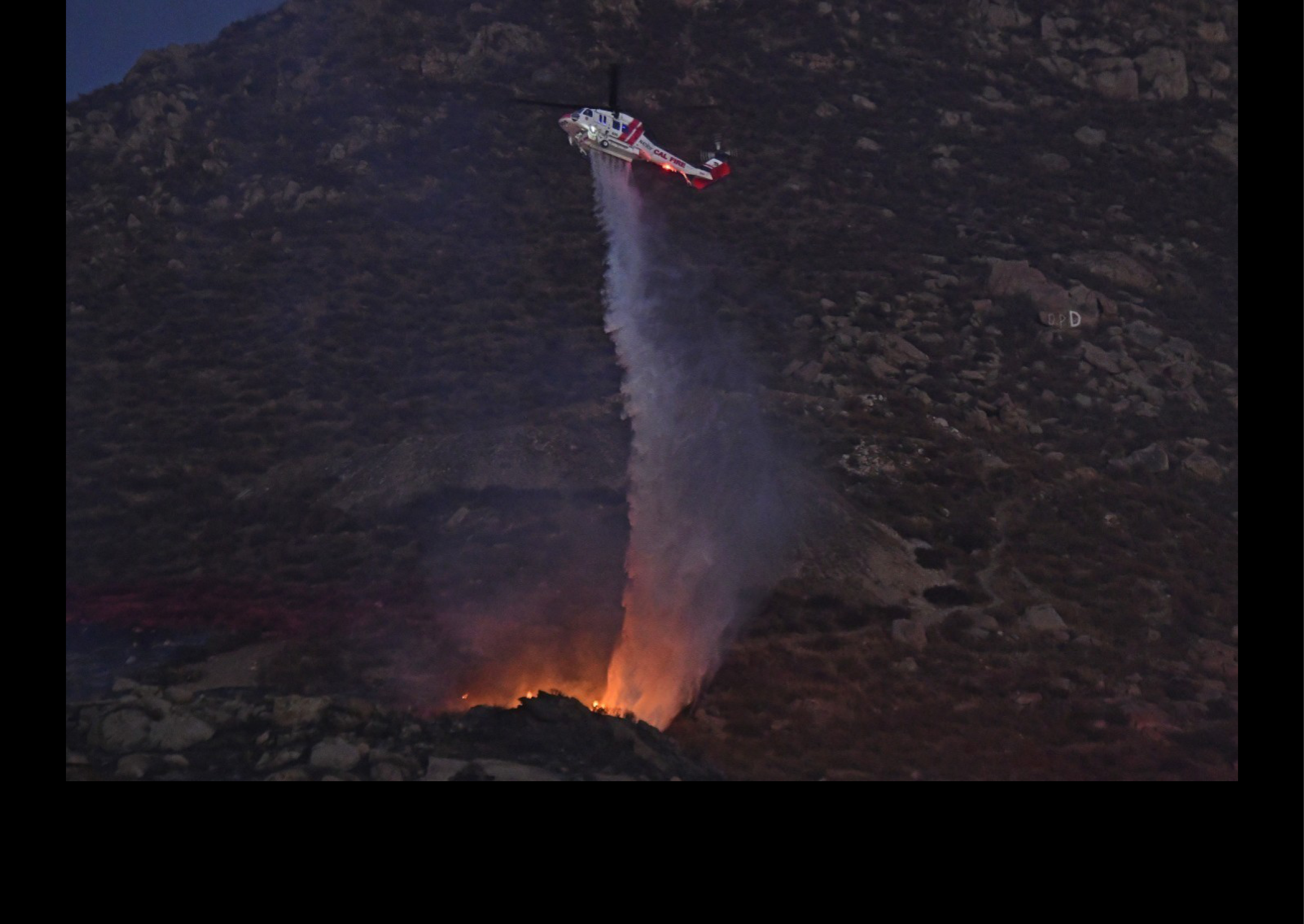 A helicopter is flying over a mountain, spraying water on a fire. AI generated content
