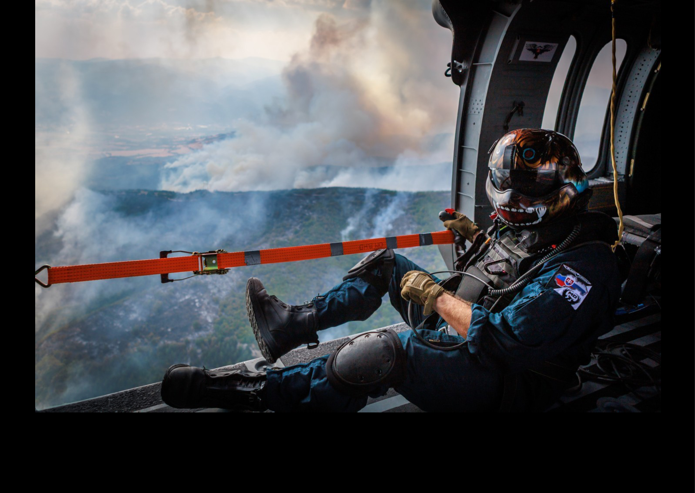 A man wearing a helmet is sitting in a helicopter, looking out at a forest fire. AI generated content