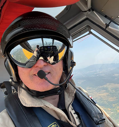 A man in a tan jacket stands in front of a yellow airplane. AI generated content