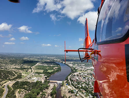 A U.S. Coast Guard MH-65 Dolphin helicopter aircrew conducts a flyover, July 10, 2025, above Kerrville, Texas. The aircrew was relieved shortly afterward by an incoming aircrew to maintain a continuous asset presence in the wake of the catastrophic flash flooding near Kerrville. (U.S. Coast Guard photo by Petty Officer 3rd Class Carmen Caver)
