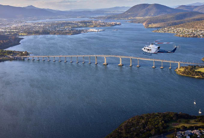 A helicopter is flying over a bridge that spans a large body of water. AI generated content
