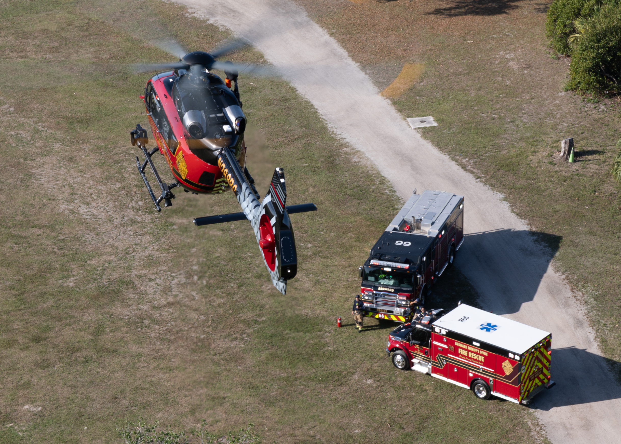 A red and black helicopter is hovering above a red and white fire truck. AI generated content