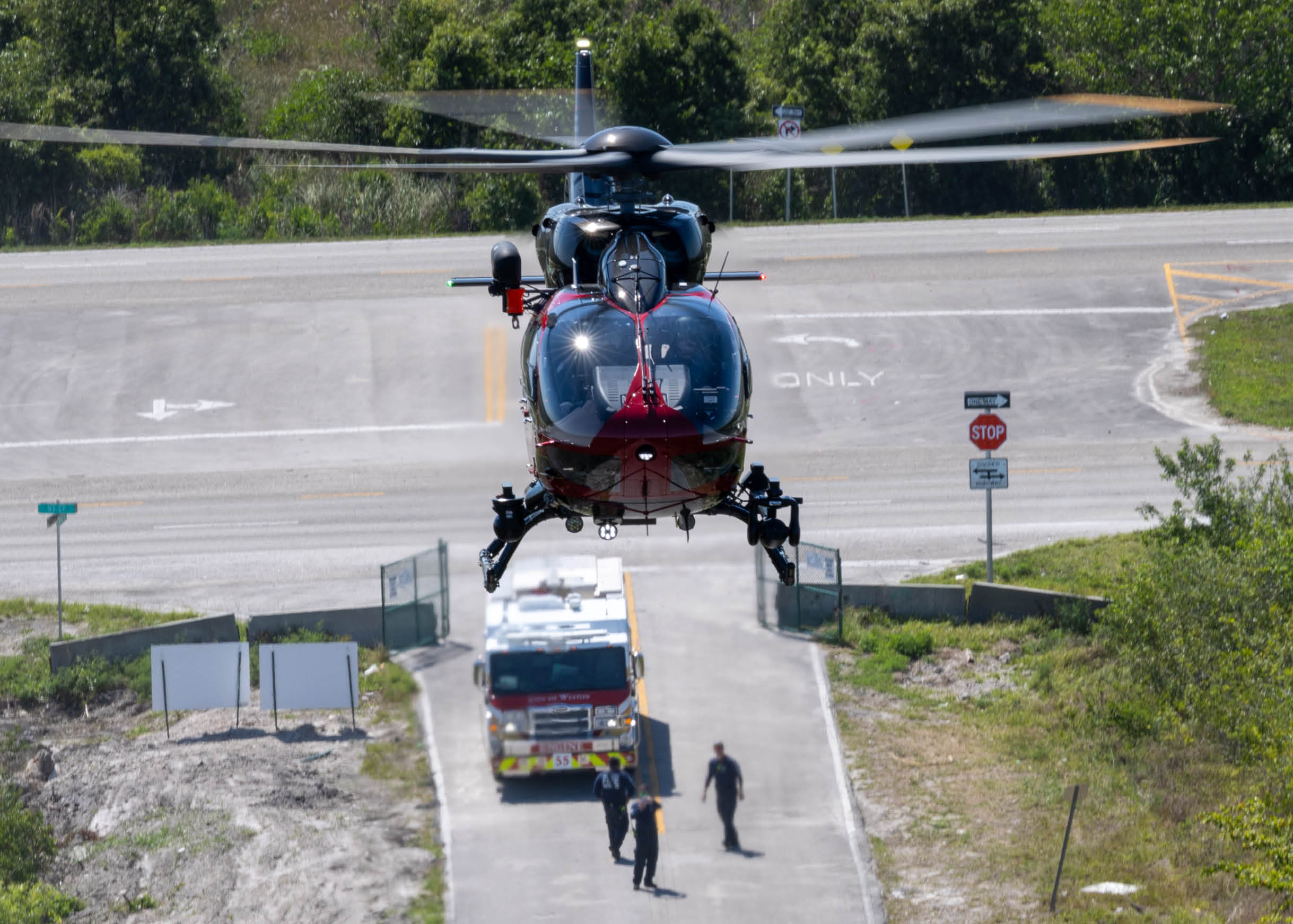 A helicopter is flying over a road with a fire truck and two men standing on the side of the road. AI generated content