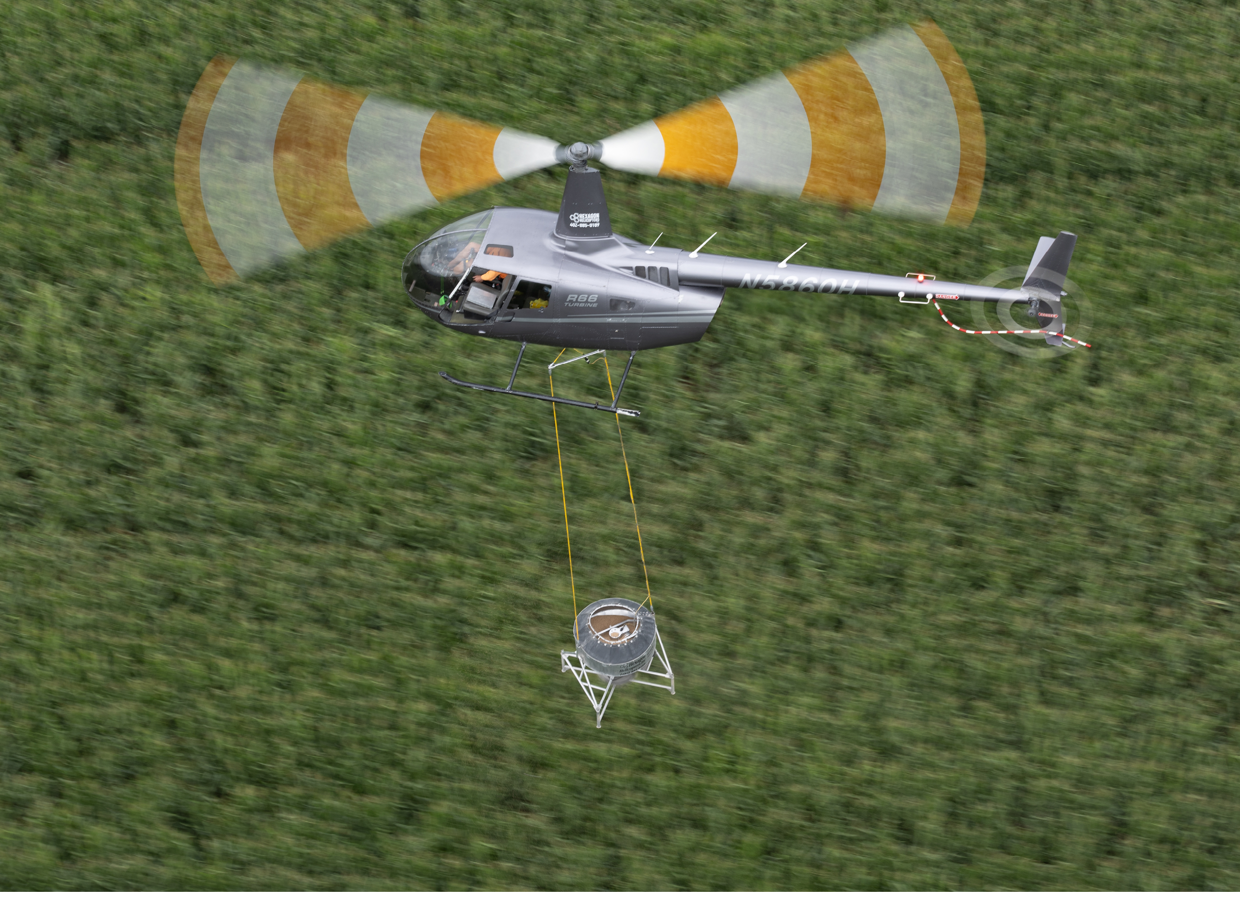 A helicopter is flying over a field with a small object hanging from it. AI generated content
