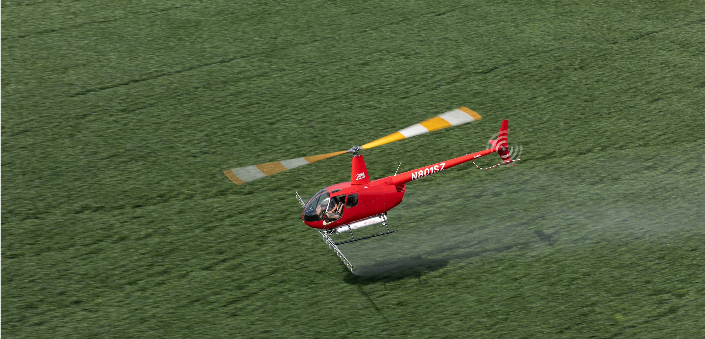 A red helicopter is flying over a grassy field, spraying water. AI generated content