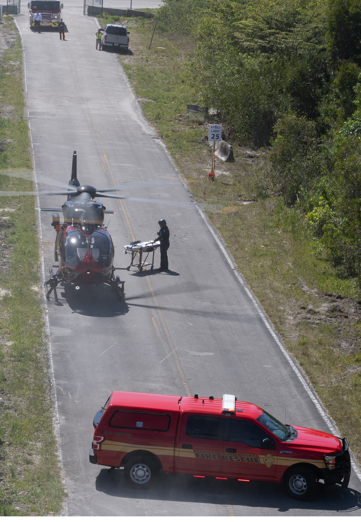 A red ambulance is parked on the side of a road, with a man standing next to it. A helicopter is also present in the scene. AI generated content