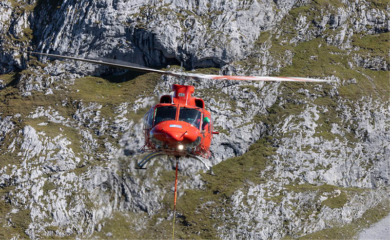 A red helicopter is flying over a rocky mountain, possibly providing support or rescue services. AI generated content