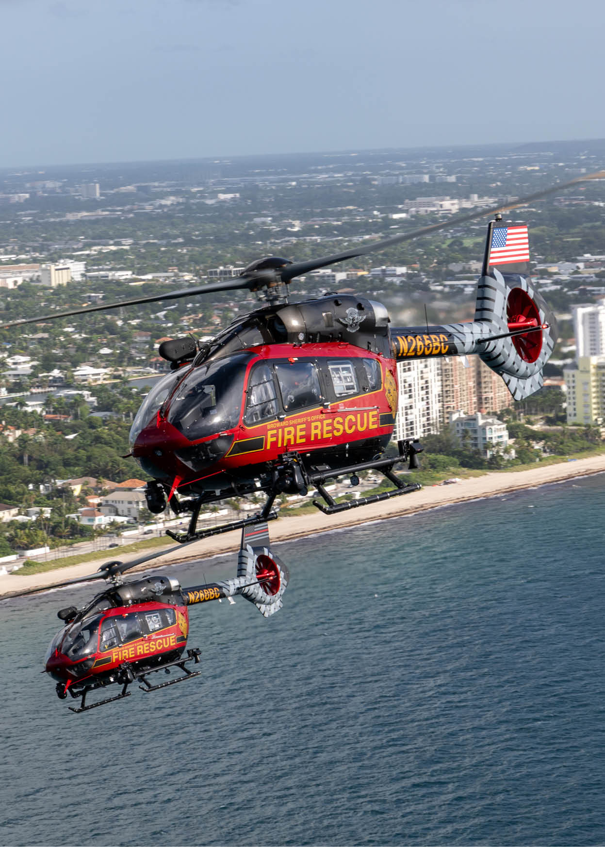 Two helicopters flying over the ocean, one is red and yellow and the other is black and red. AI generated content